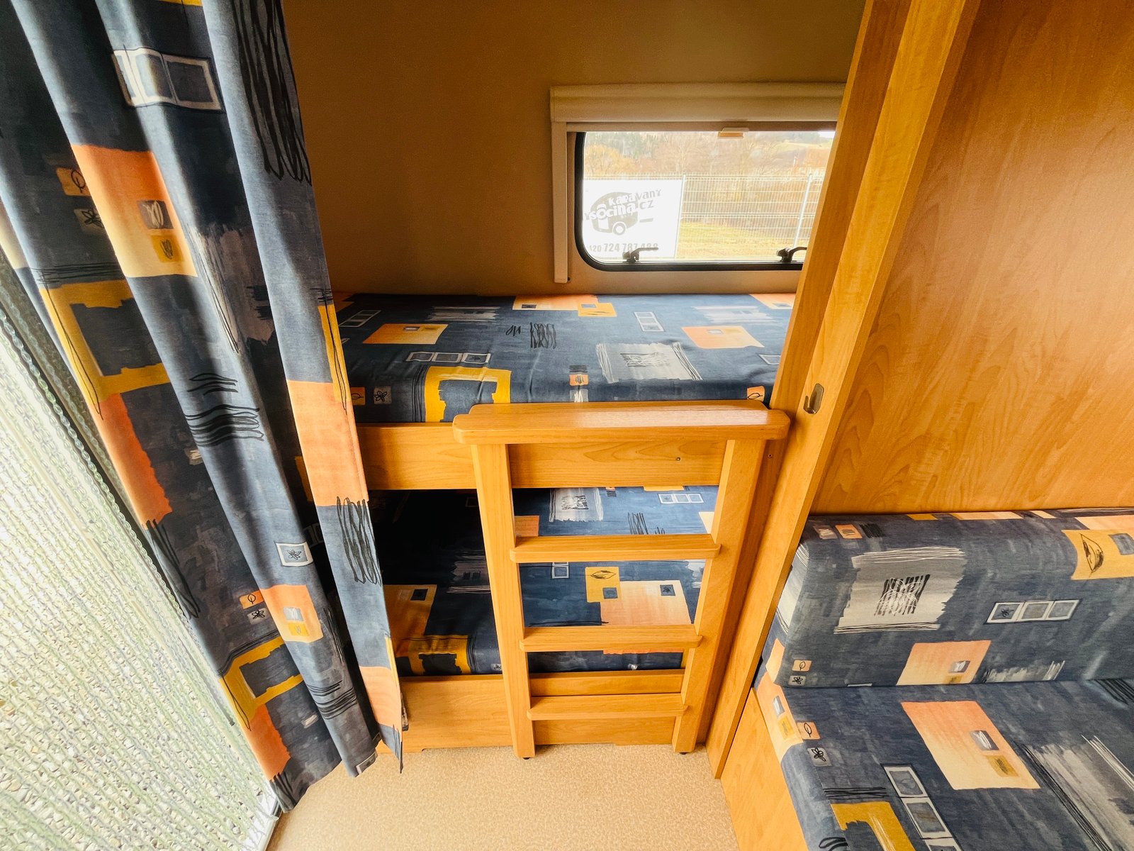Interiér karavanu s pohodlnými lůžky a stylovými záclonami. Ideální pro rodinné výlety a relaxaci na cestách.