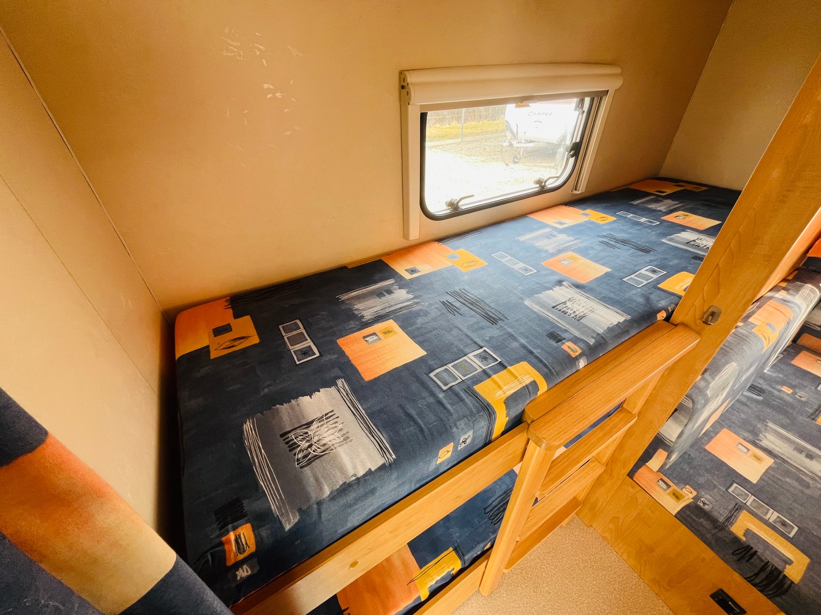 Obrázek interiéru karavanu s pohodlnými vyvýšenými postelemi a barevnými potahy. Komfort pro vaši cestu!