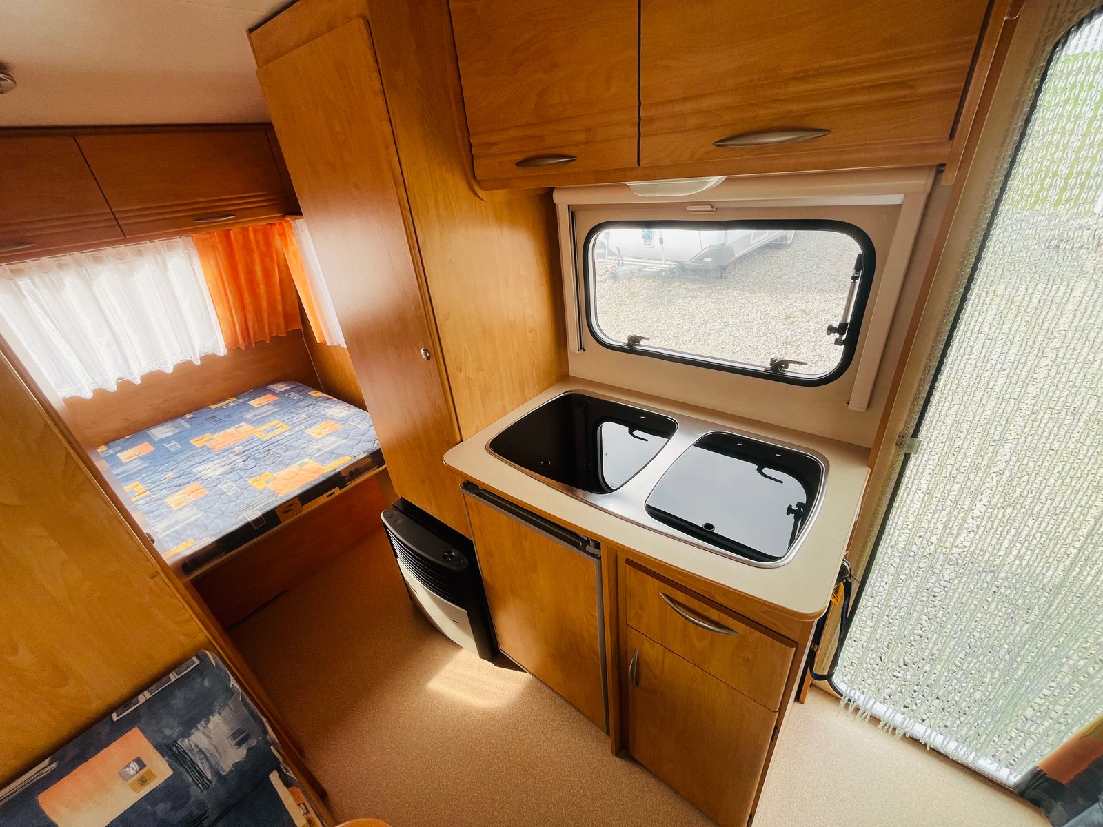 Interiér karavanu s kuchyňkou a spací zónou, dřevo, praktické uspořádání. Ideální pro pohodlné cestování.