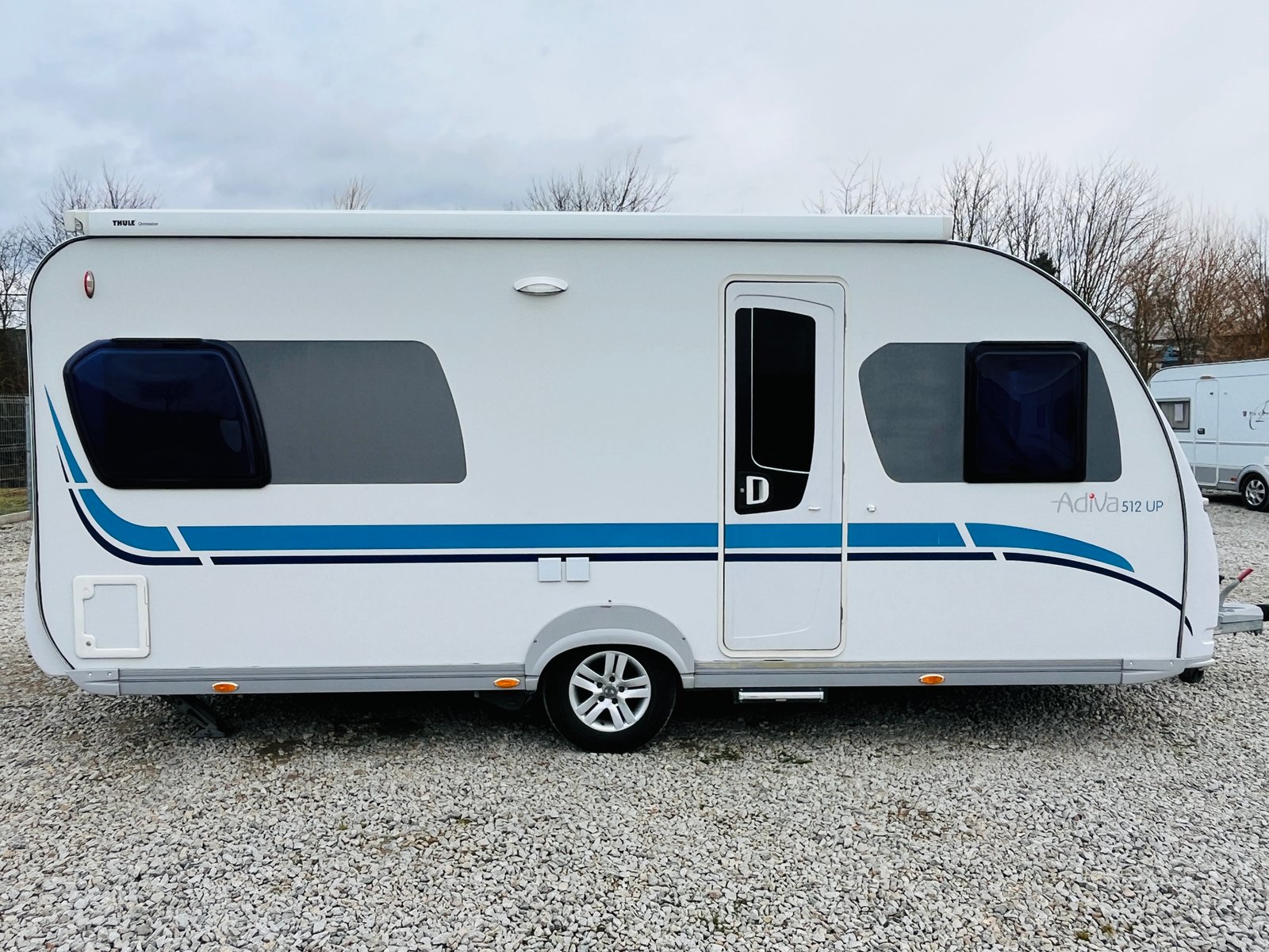 Karavan Adria 512 UP s moderním designem a bílou karoserií ve stylu s modrými detaily.