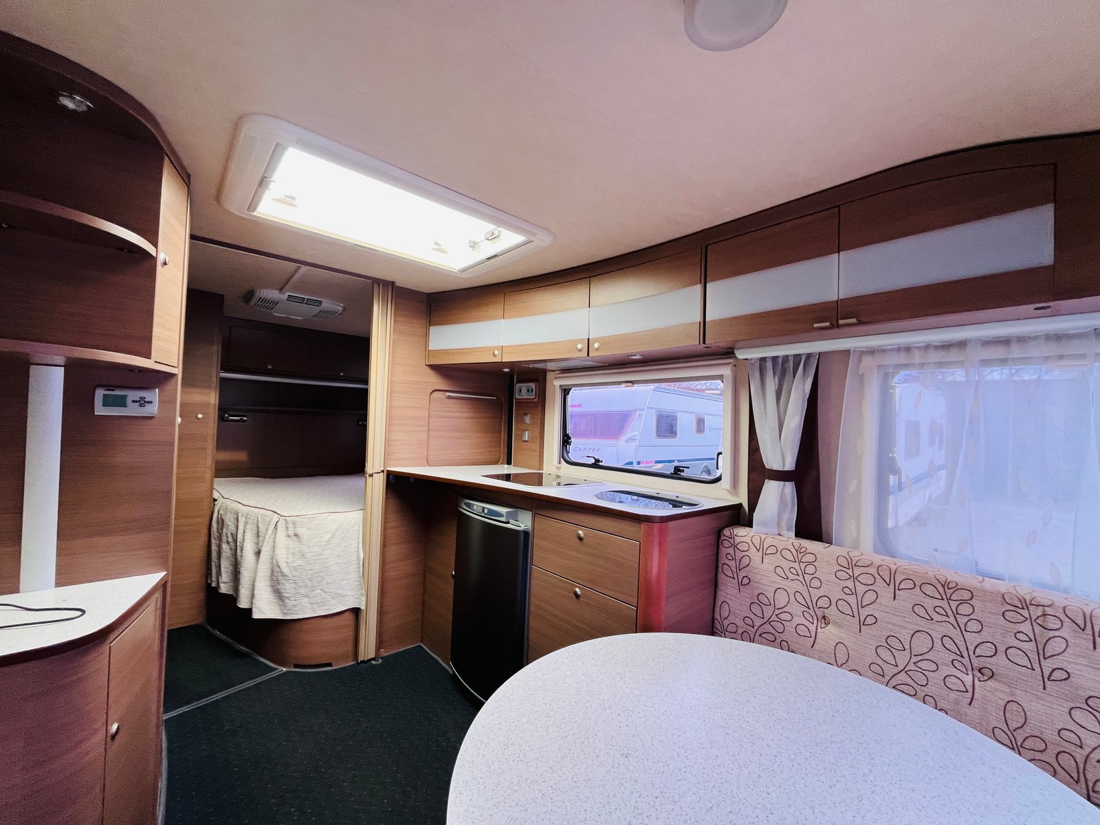 Interiér karavanu s kuchyňkou a ložnicí. Moderní design, dřevěné prvky a dostatek úložného prostoru.