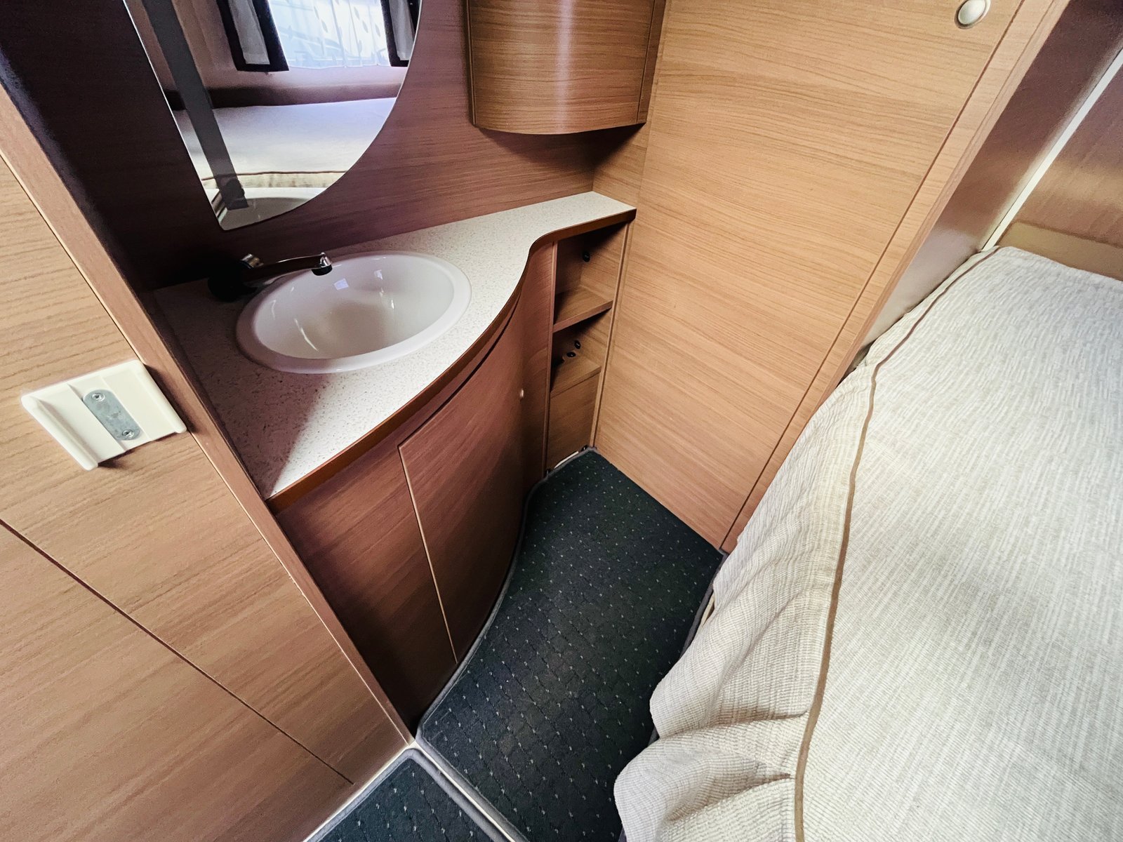 Obrázek interiéru karavanu, který zobrazuje koupelnový kout s umyvadlem a úložnými prostory.