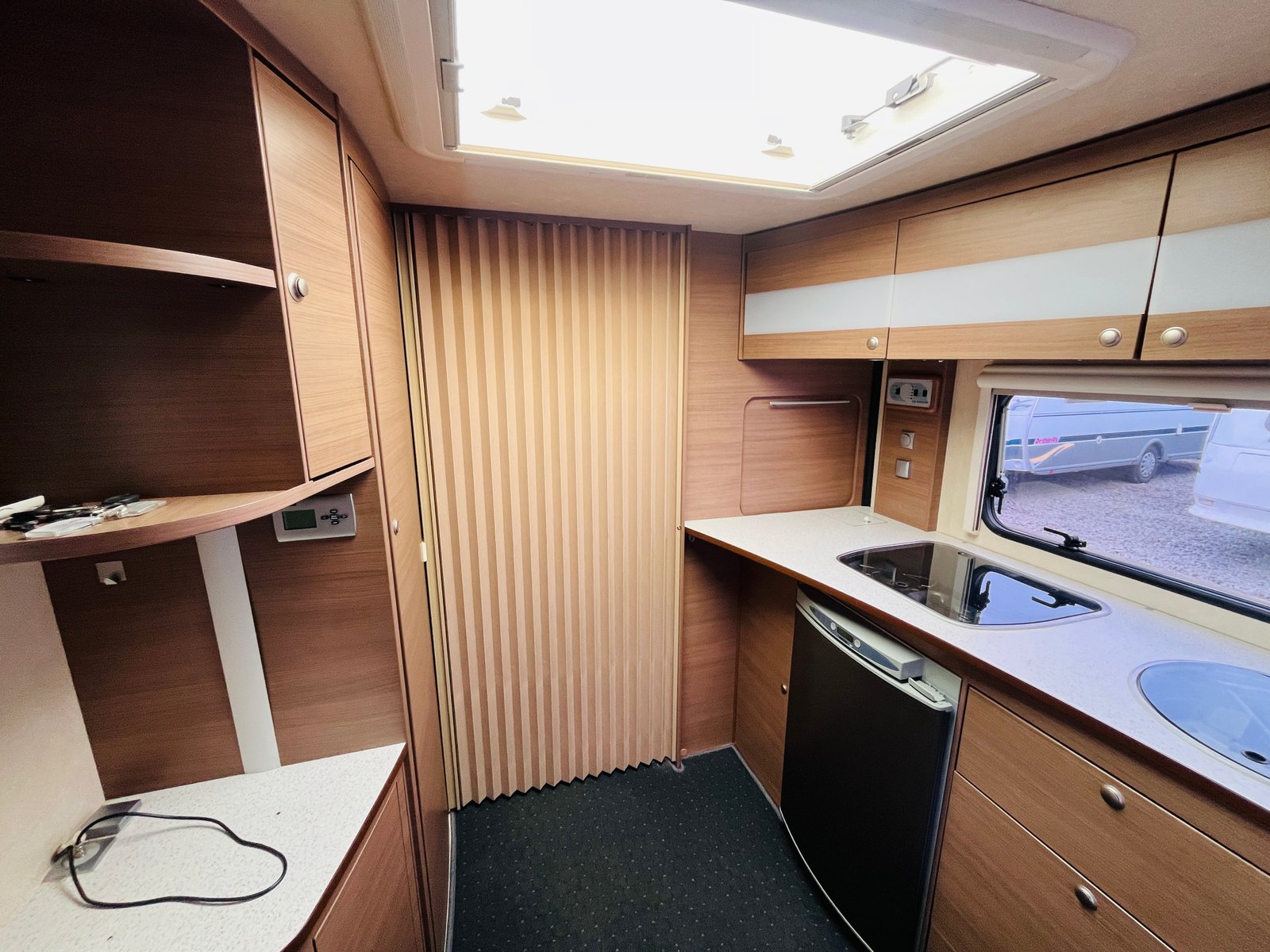 Obrázek interiéru karavanu s moderním zařízením a kuchyňským koutem. Stylové dřevěné dekory a úložné prostory.