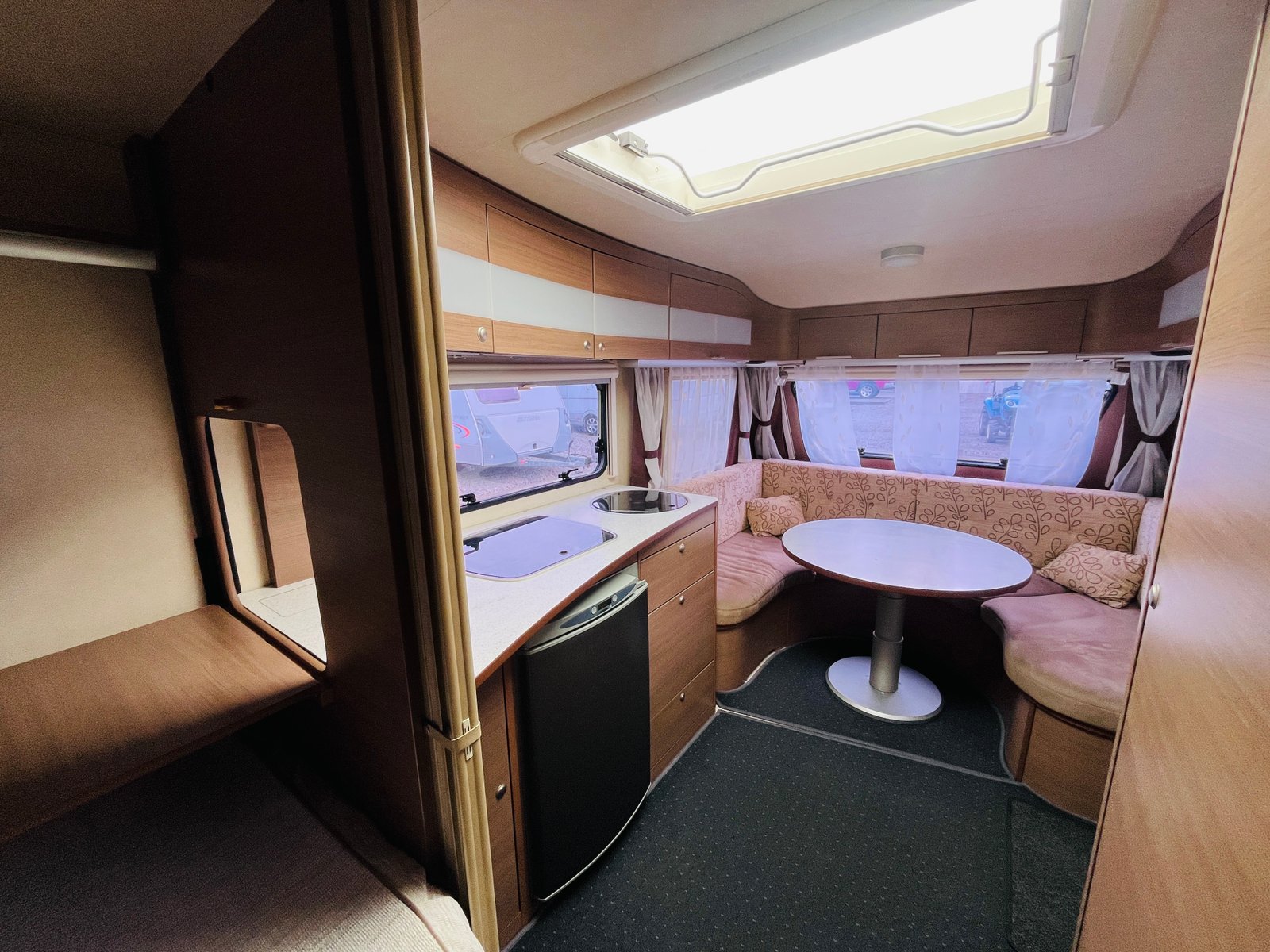 Obrázek interiéru karavanu s kuchyní, stolem a pohodlným posezením. Ideální pro cestování a relaxaci.