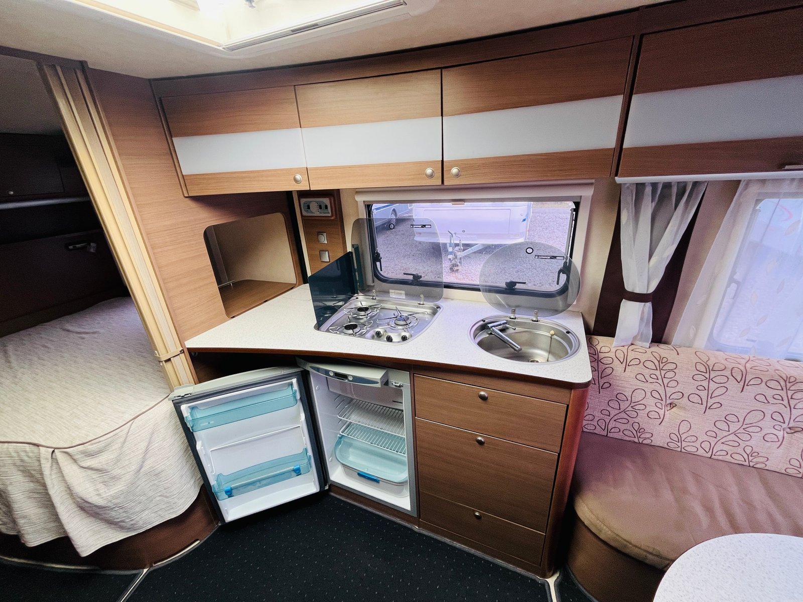 Interiér karavanu s kuchyní a ložním prostorem, ideální pro pohodlné cestování.