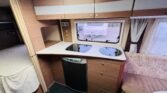 Interiér karavanu s kuchyňským koutem, skříněmi a pohodlným sezením. Ideální pro cestování a odpočinek.