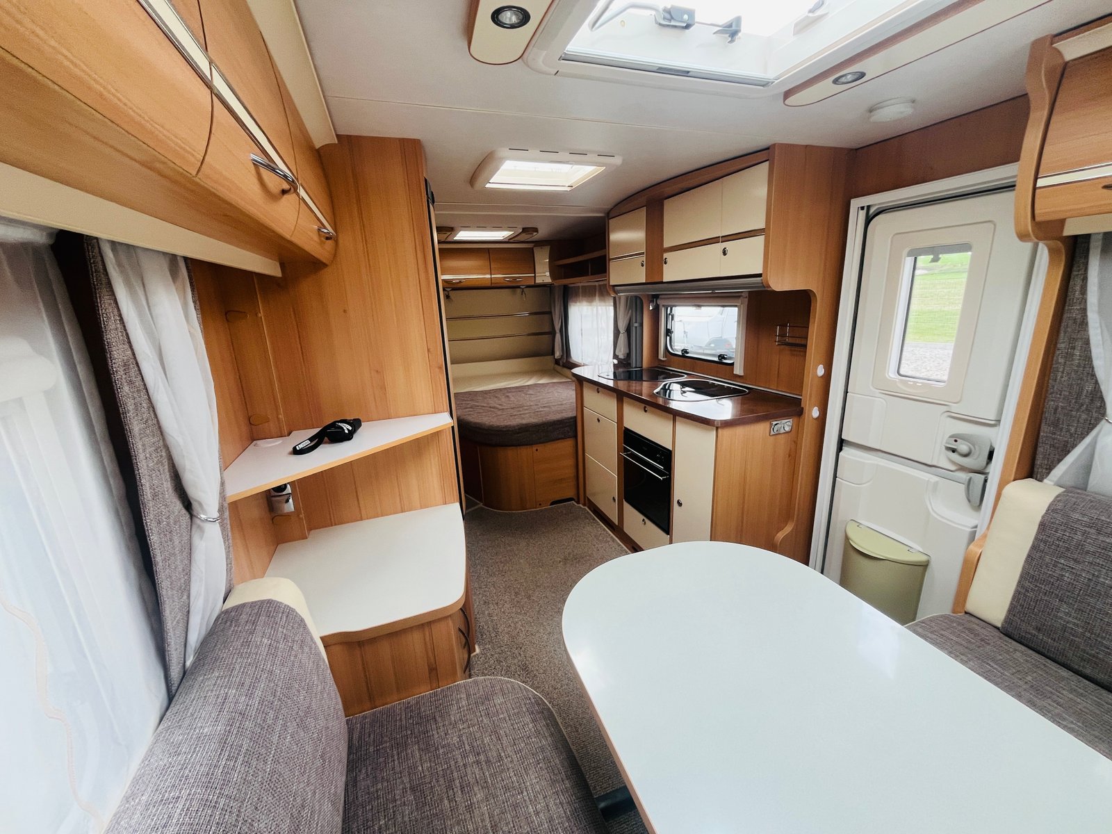 Obrázek interiéru karavanu. Moderní, dřevěné obložení, kuchyňský kout a pohodlné posezení. Ideální pro dovolenou.