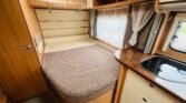Interiér karavanu s pohodlným lůžkem a kuchyňkou. Ideální pro rodinné kempaření.