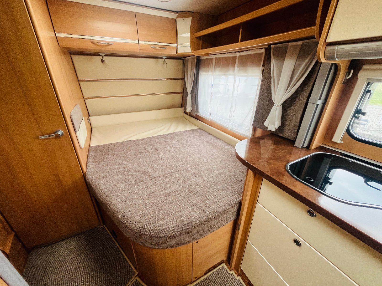 Interiér karavanu s pohodlným lůžkem a kuchyňkou. Ideální pro rodinné kempaření.