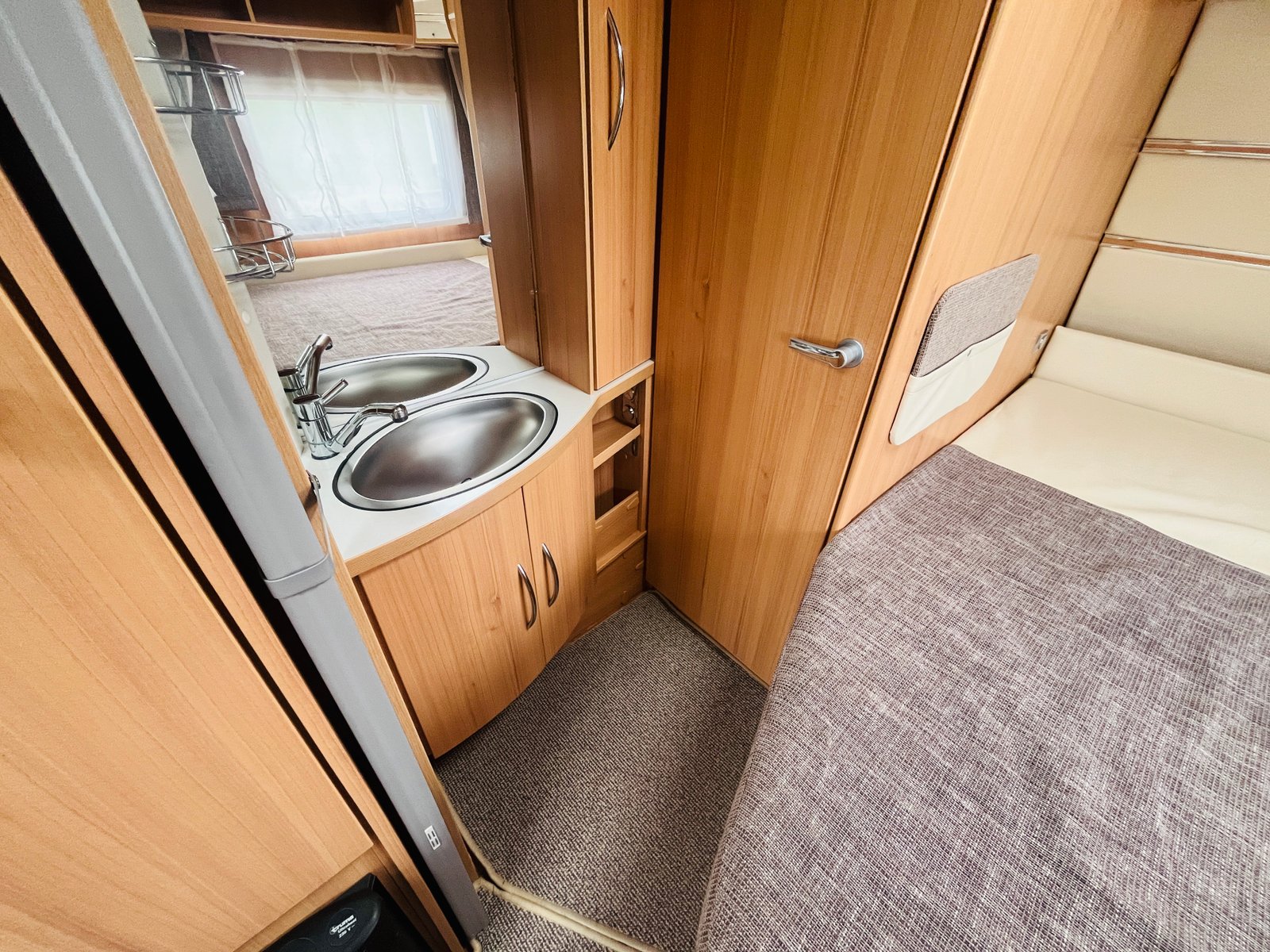 Obrázek interiéru karavanu s kuchyňským koutem a ložkem, teplé dřevěné detaily pro pohodovou atmosféru.