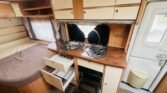 Interiér karavanu s kuchyňkou a místem na spaní. Funkční a útulný design pro pohodlné cestování.
