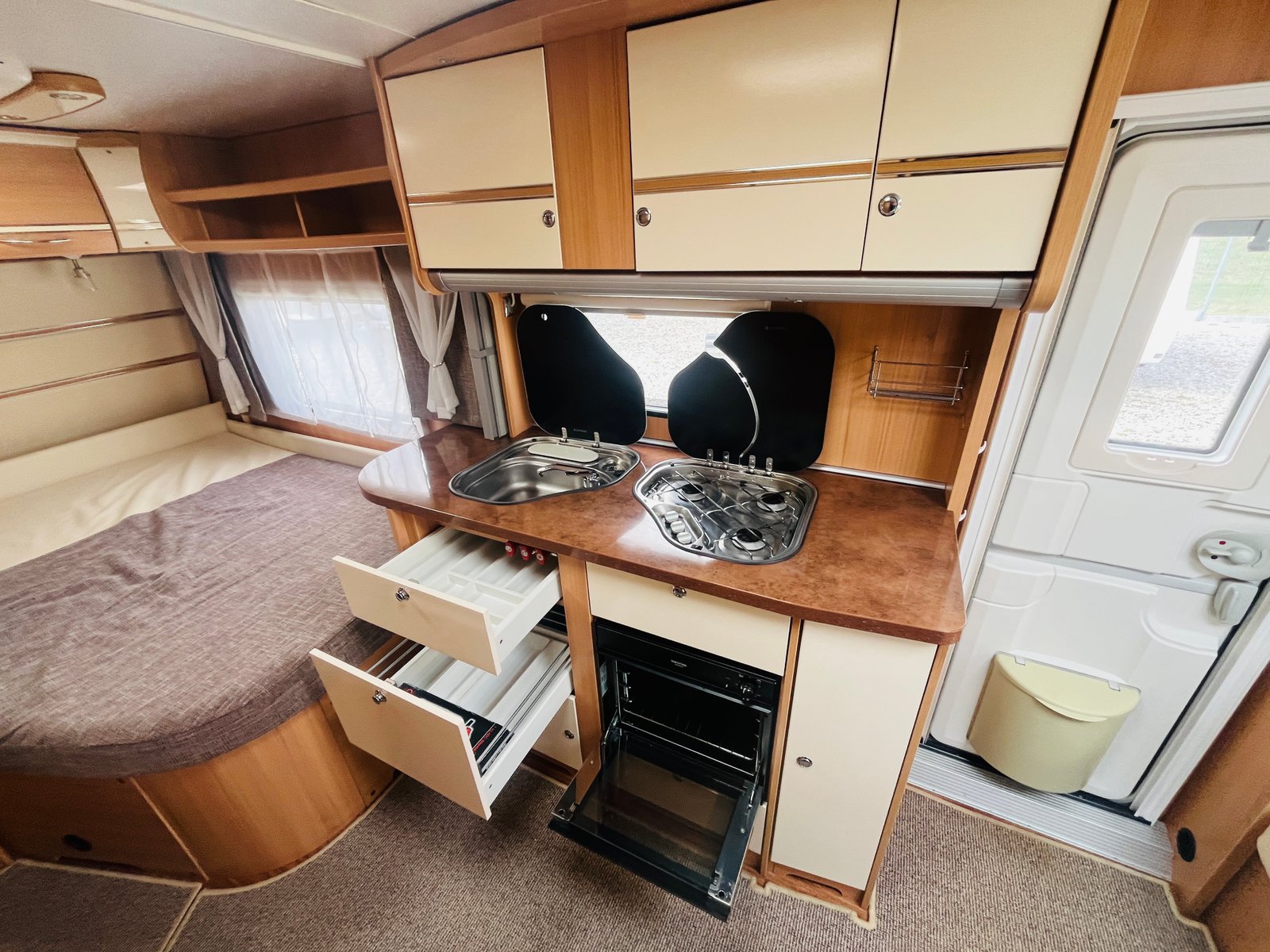 Interiér karavanu s kuchyňkou a místem na spaní. Funkční a útulný design pro pohodlné cestování.