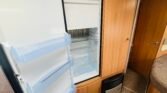 Obrázek zobrazující lednici v interiéru karavanu. Útulný prostor s dřevěným nábytkem.