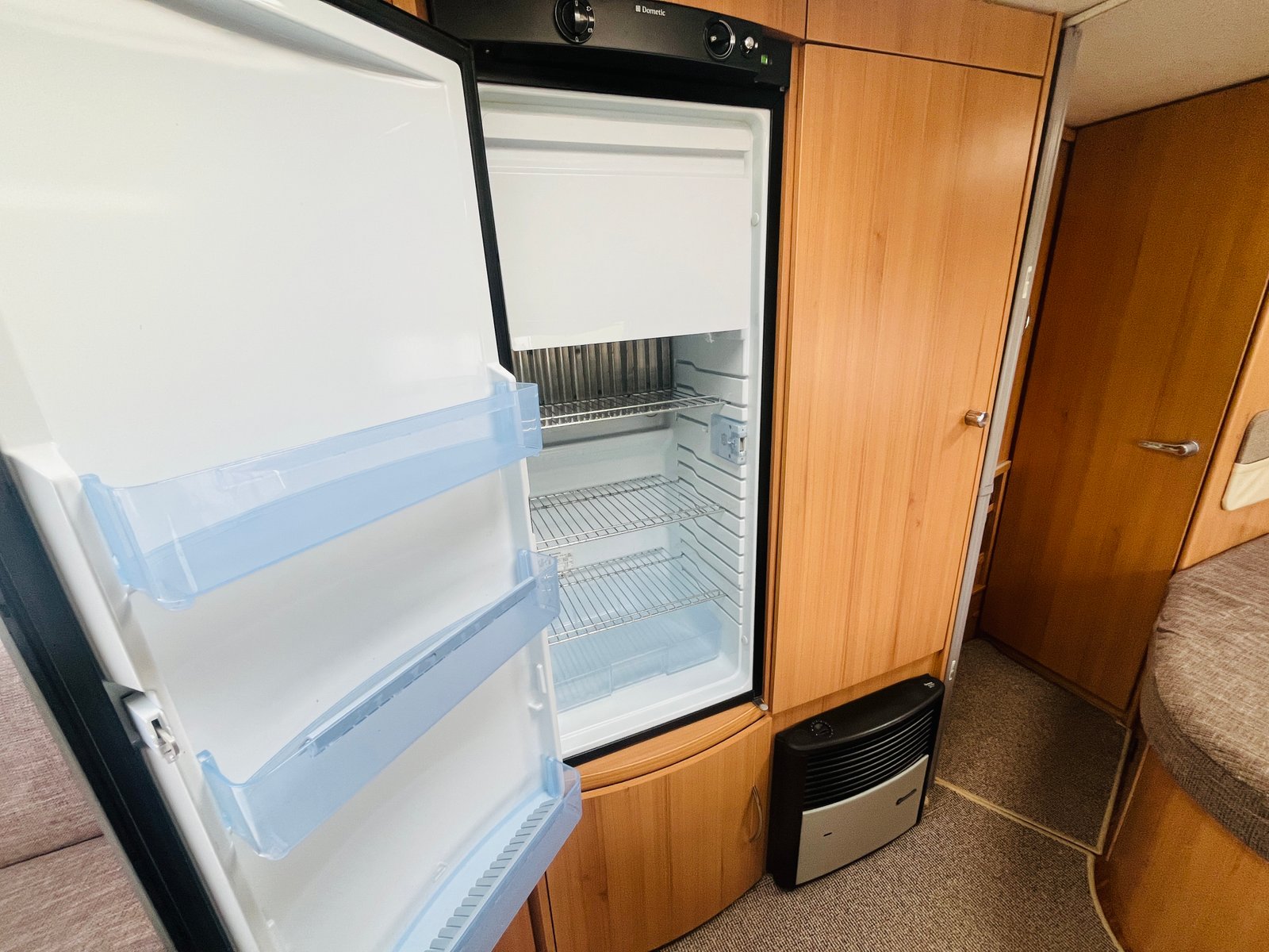 Obrázek zobrazující lednici v interiéru karavanu. Útulný prostor s dřevěným nábytkem.