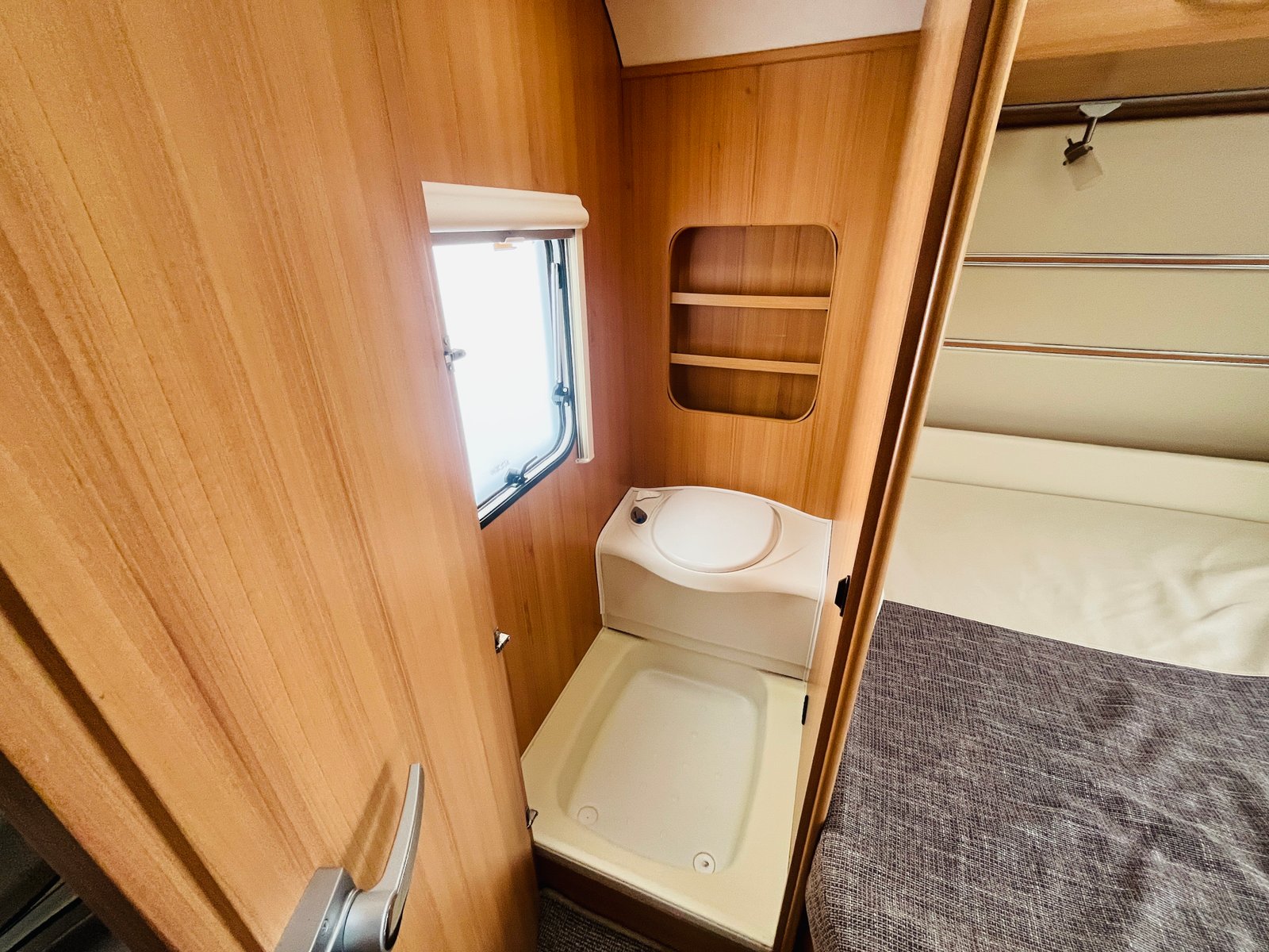 Interiér karavanu s toaletou a dřevěnými prvky, moderní a praktický design pro pohodlné kempování.