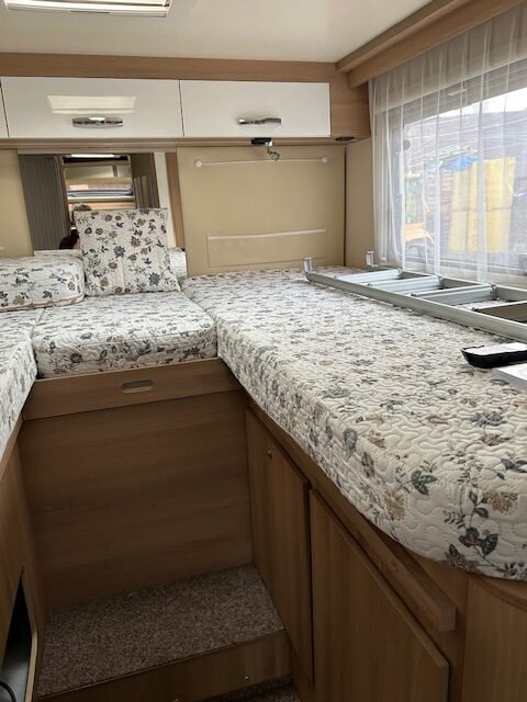 Interiér obytného auta s prostornými lůžky a dřevěnými elementy. Komfort pro cestování i odpočinek.