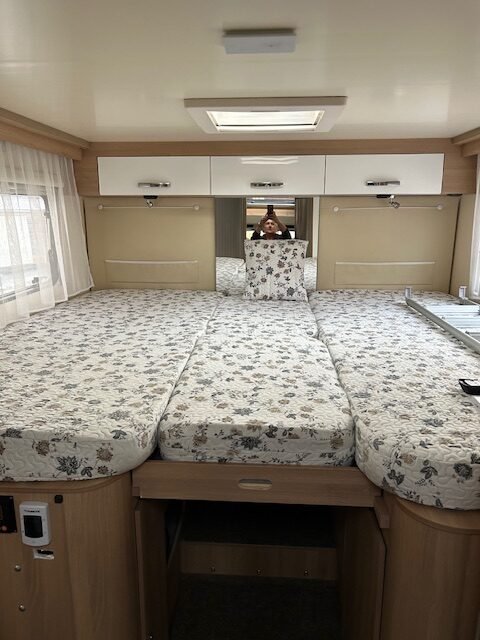 Interiér karavanu s prostornou ložnicí a pohodlnými matracemi potaženými květinovým vzorem.