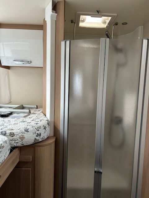 Obrázek interiéru obytného auta s odděleným sprchovým koutem a pohodlným lůžkem. Ideální pro pohodlné cestování.