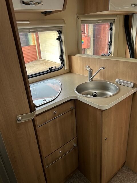 Moderní karavan s kuchyňským koutem, dřezem a úložnými skříňkami. Ideální pro pohodlné cestování.