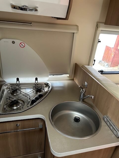 Kuchyňka karavanu s vařičem a dřezem, ideální pro přípravu jídel na cestách. Komfort a funkčnost na prvním místě!