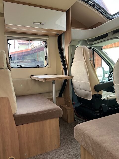 Obrázek interiéru obytného auta s rozkládacím stolem a pohodlnými sedačkami. Ideální pro dobrodružství na cestách.