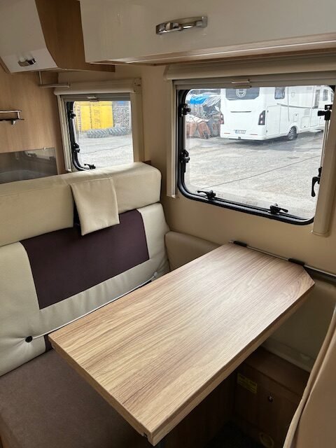 Obrázek interiéru karavanu s dřevěným stolem a pohodlnými sedadly. Ideální pro pohodlné cestování.