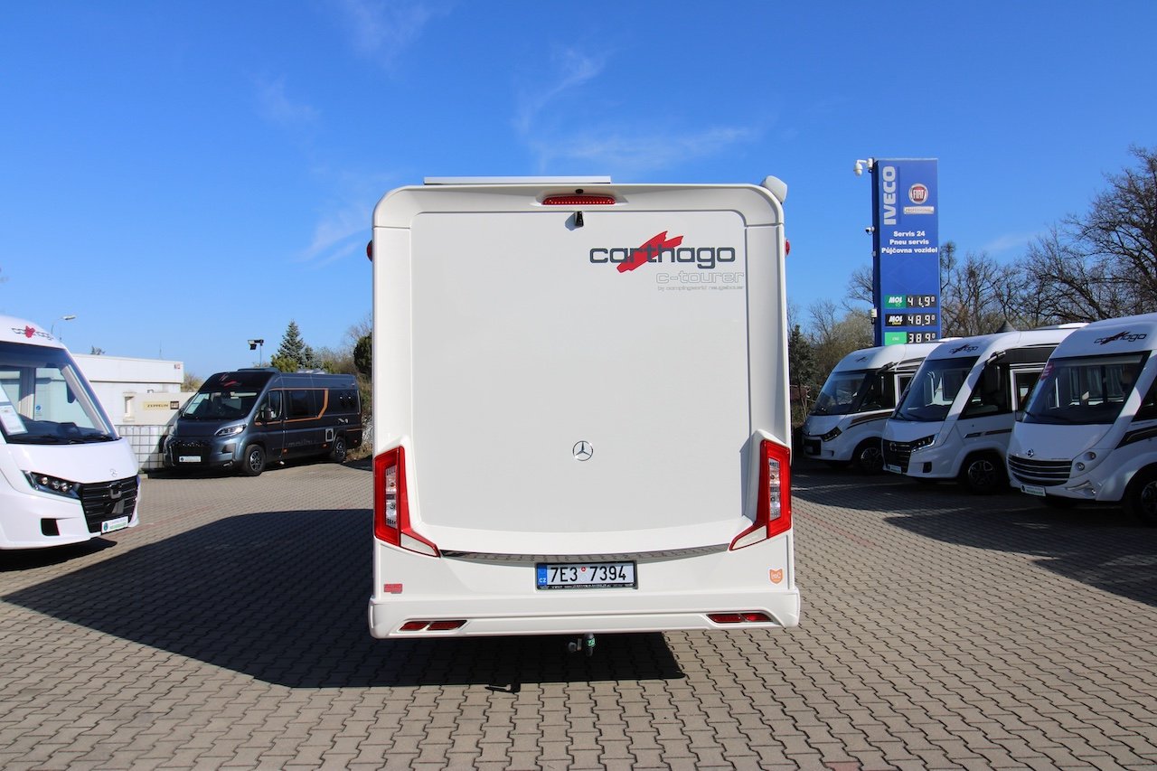 Obytné auto Carthago e-tourer zaparkované na prodejní ploše s modrou oblohou a dalšími vozidly v pozadí.