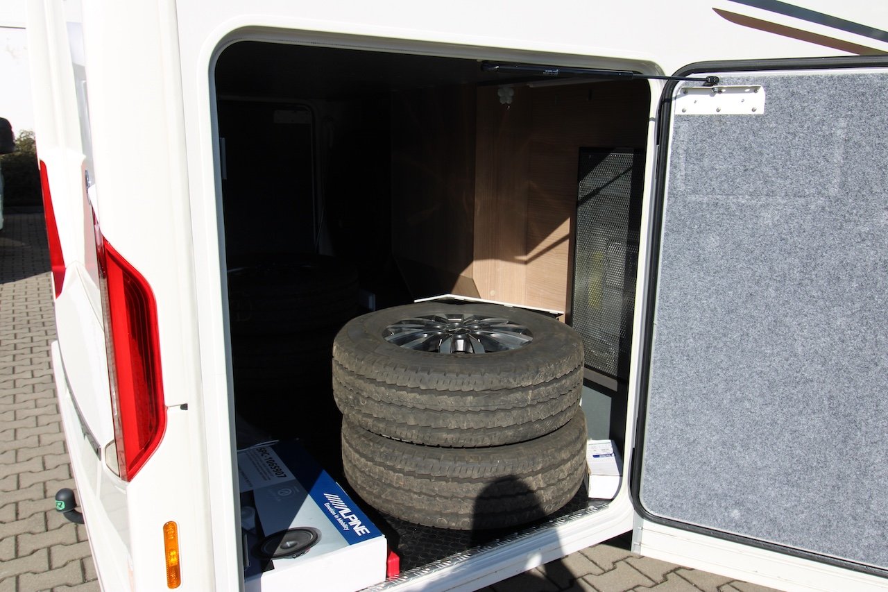 Vnitřní úložný prostor obytného auta, obsahující pneumatiky a další příslušenství.