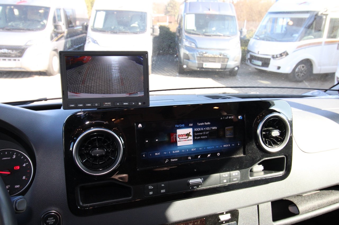 Obrázek interiéru obytného auta s moderním infotainmentem a kamerovým systémem.