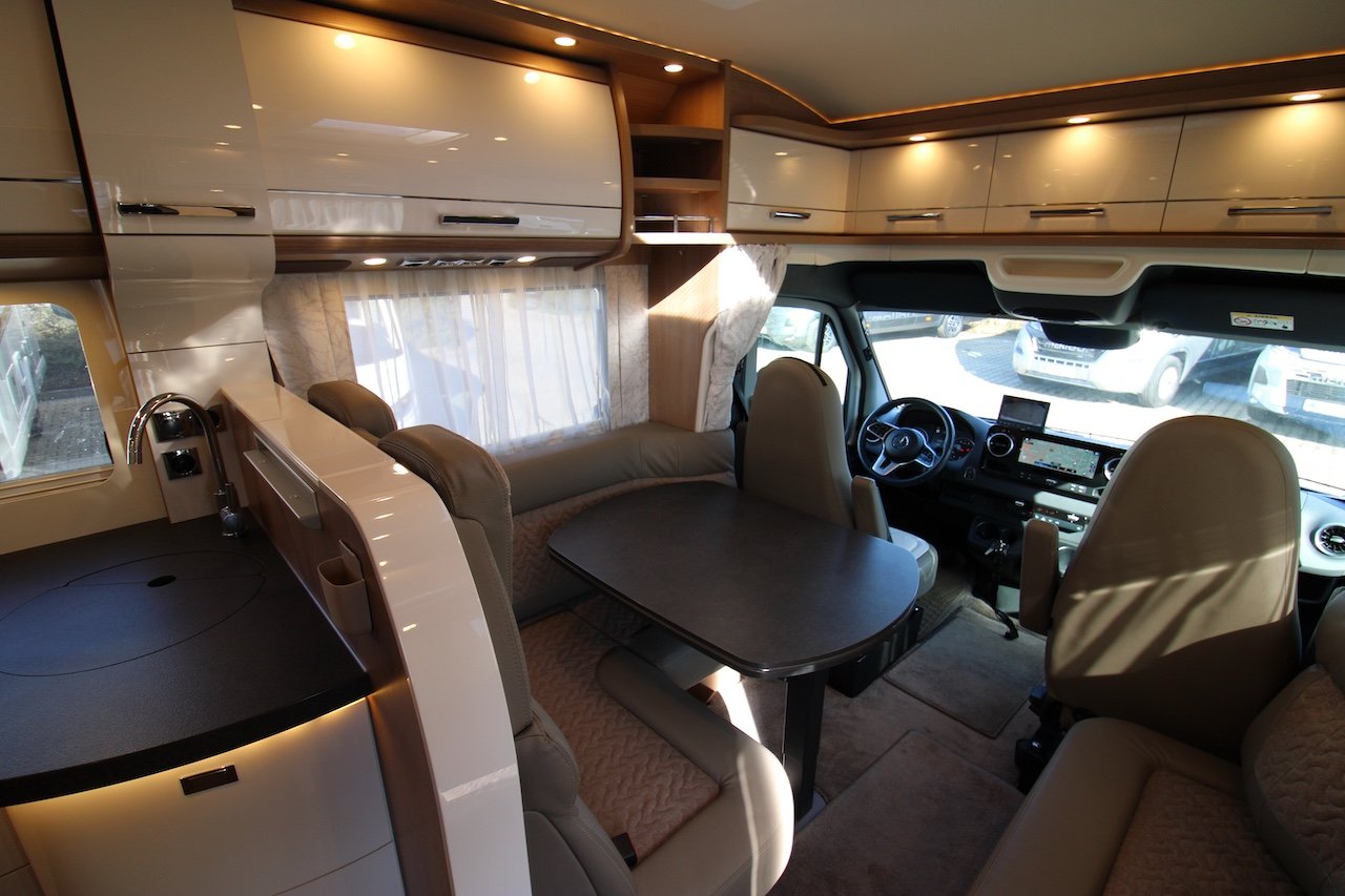 Obrázek interiéru obytného auta s pohodlným sezením a moderním kuchyňským koutem.