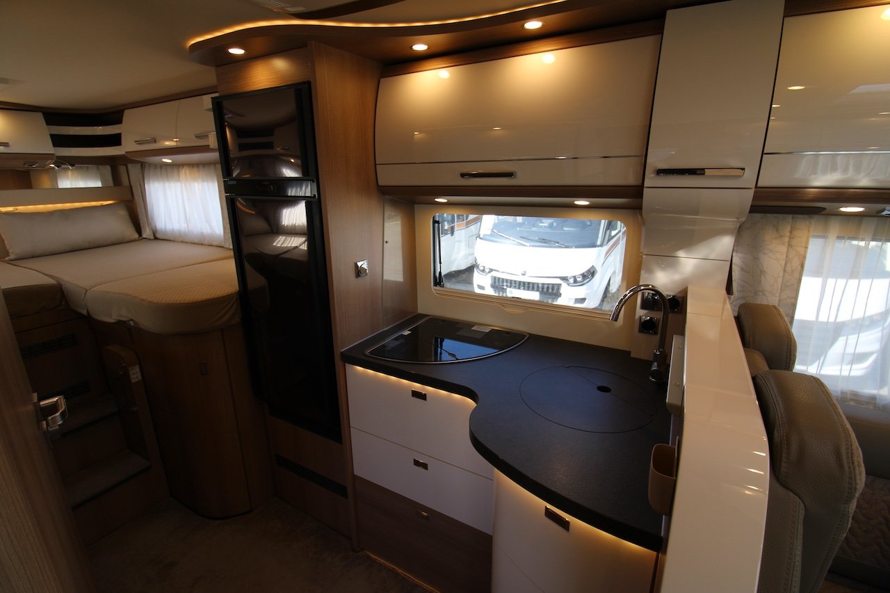 Obrázek interiéru obytného vozu s moderní kuchyní a komfortním spací prostorem.