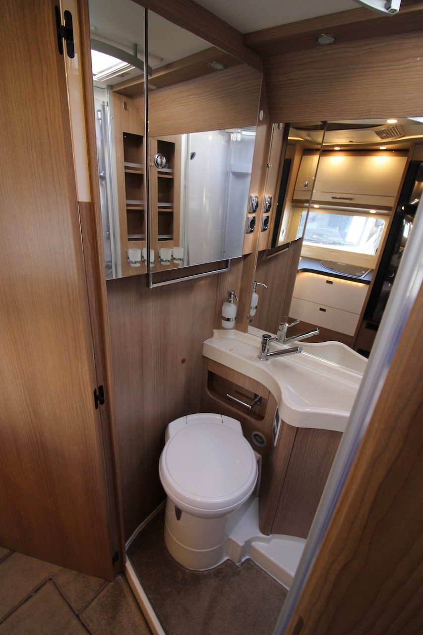 Obrázek ukazuje interiér obytného vozu s moderním sanitárním prostorem a dřezem.