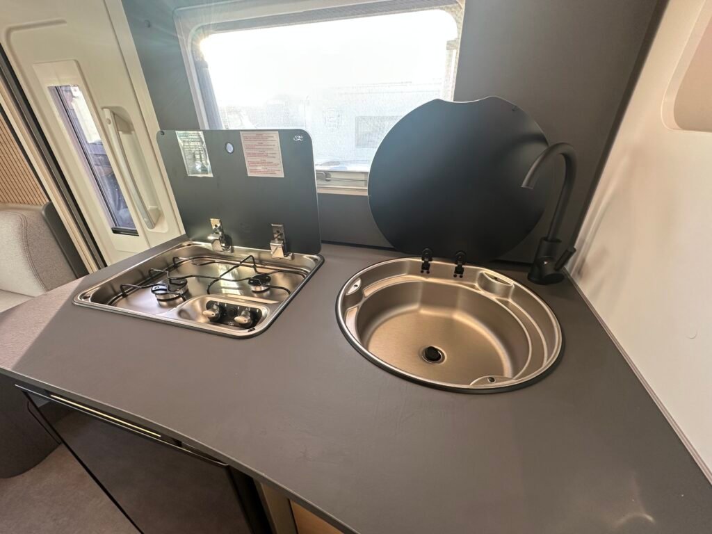 Moderní kuchyňka s dřezem a vařičem. Ideální pro obytné auto nebo karavan. Značka a model nejsou uvedeny.