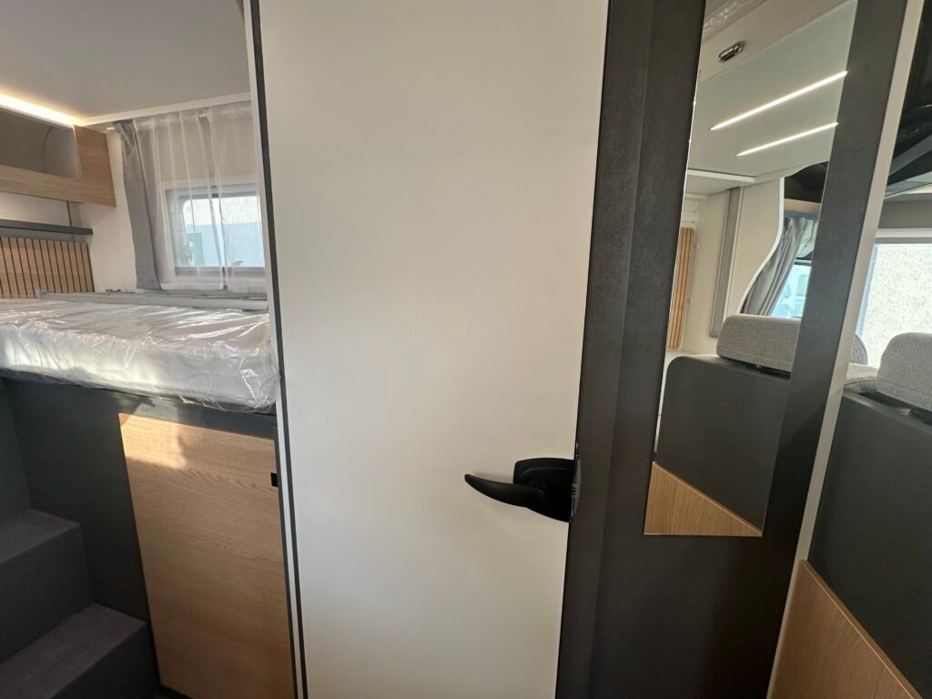 Interiér moderního obytného auta s manželskou postelí a úložným prostorem. Elegantní design pro pohodlné cestování.