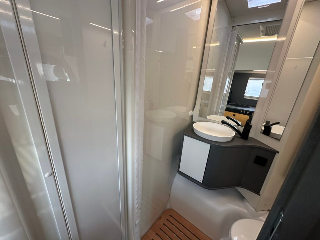 Luxusní koupelna v obytném autě, moderní design s umyvadlem a sprchovým koutem. Ideální pro pohodlné cestování!