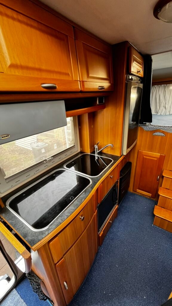 Interiér obytného vozu s dřevěným nábytkem a kuchyňským vybavením. Ideální pro pohodlné cestování.