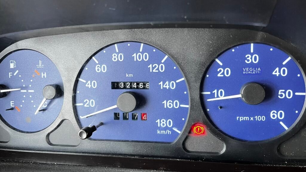 Obrázek přístrojové desky obytného auta, ukazuje tachometr a ukazatele teploty, paliva a otáček motoru.