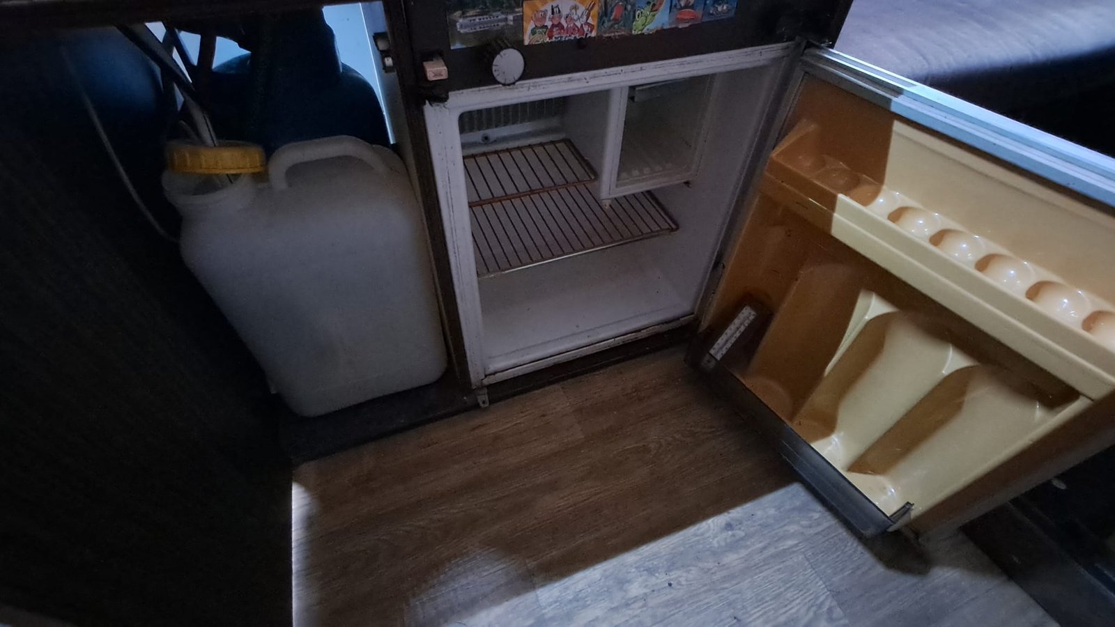 Obrázek zobrazuje lednici uvnitř obytného vozu. Interiér je přehledný s jednoduchým designem.