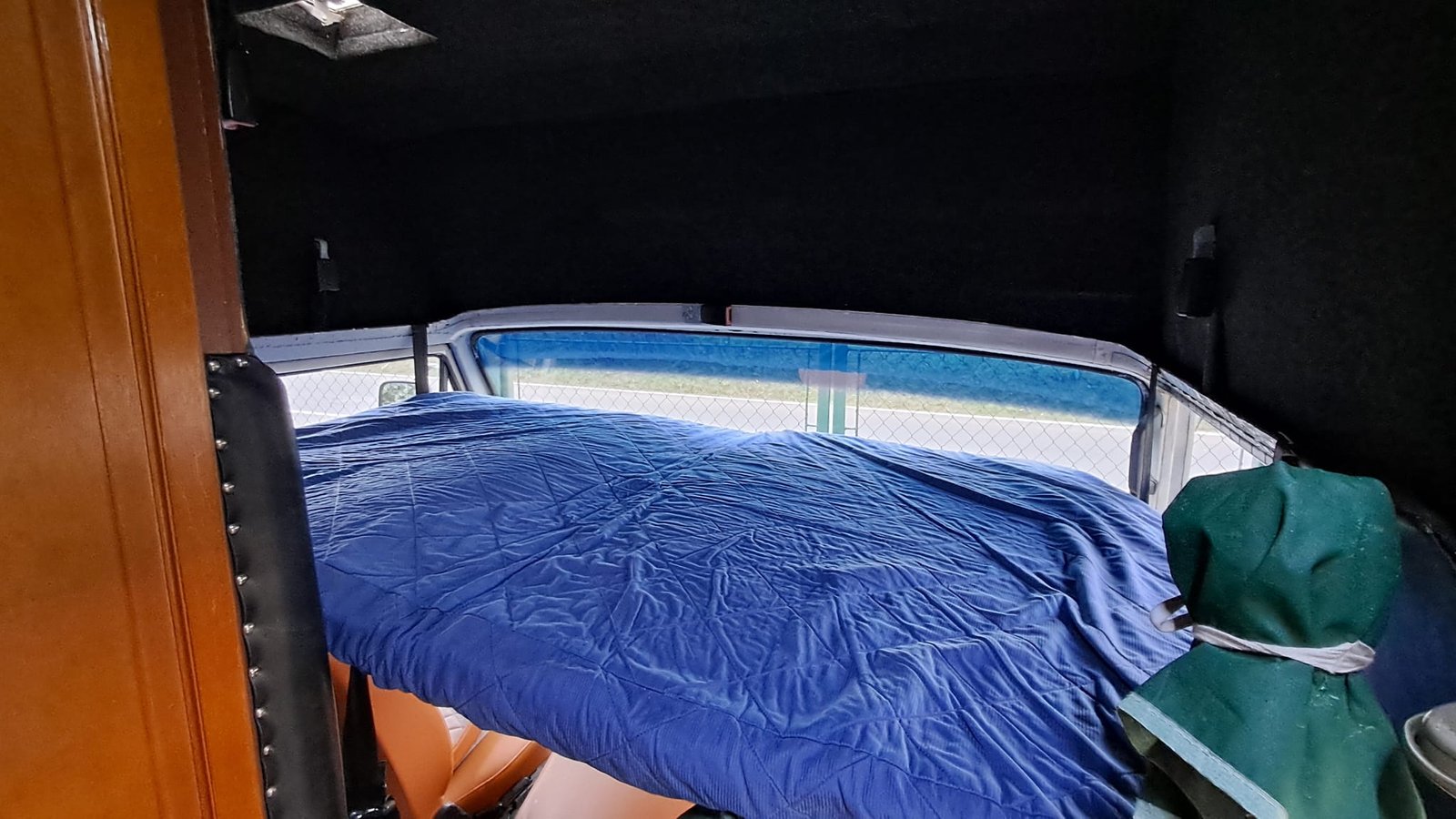 Obrázek interiéru obytného auta s modrou přikrývkou a výhledem na okno. Komfortní místo pro odpočinek nebo spánek.
