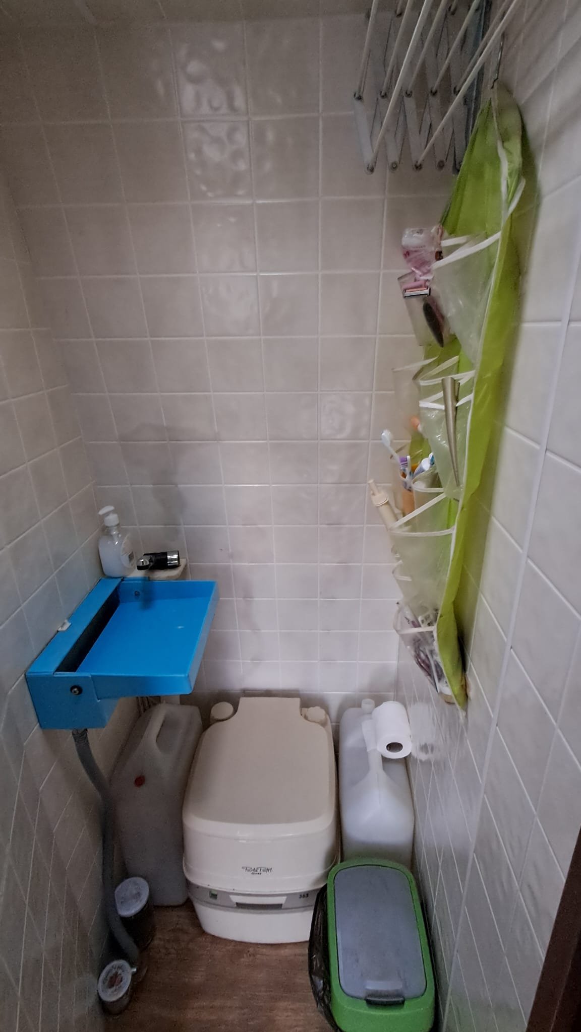 Obrázek interiéru karavanu se záchodem a umyvadlem. Design zahrnuje modrou skříňku a úložné prostory.