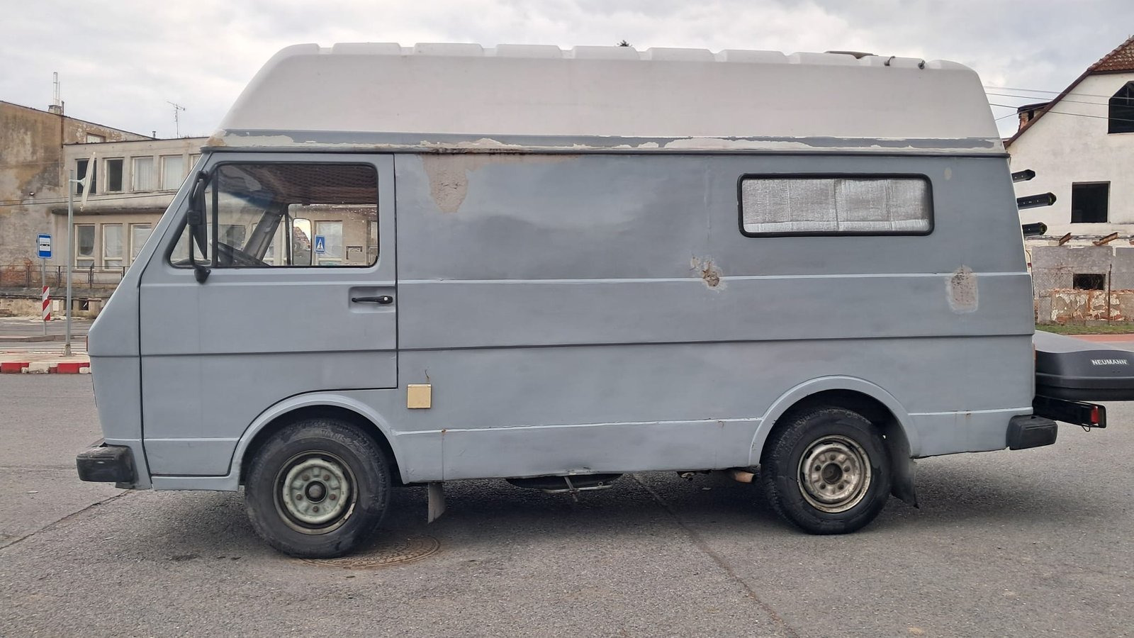 Obytné auto, šedé barvy, bez zjevné značky a modelu, s jednoduchým designem a úložným prostorem vzadu.