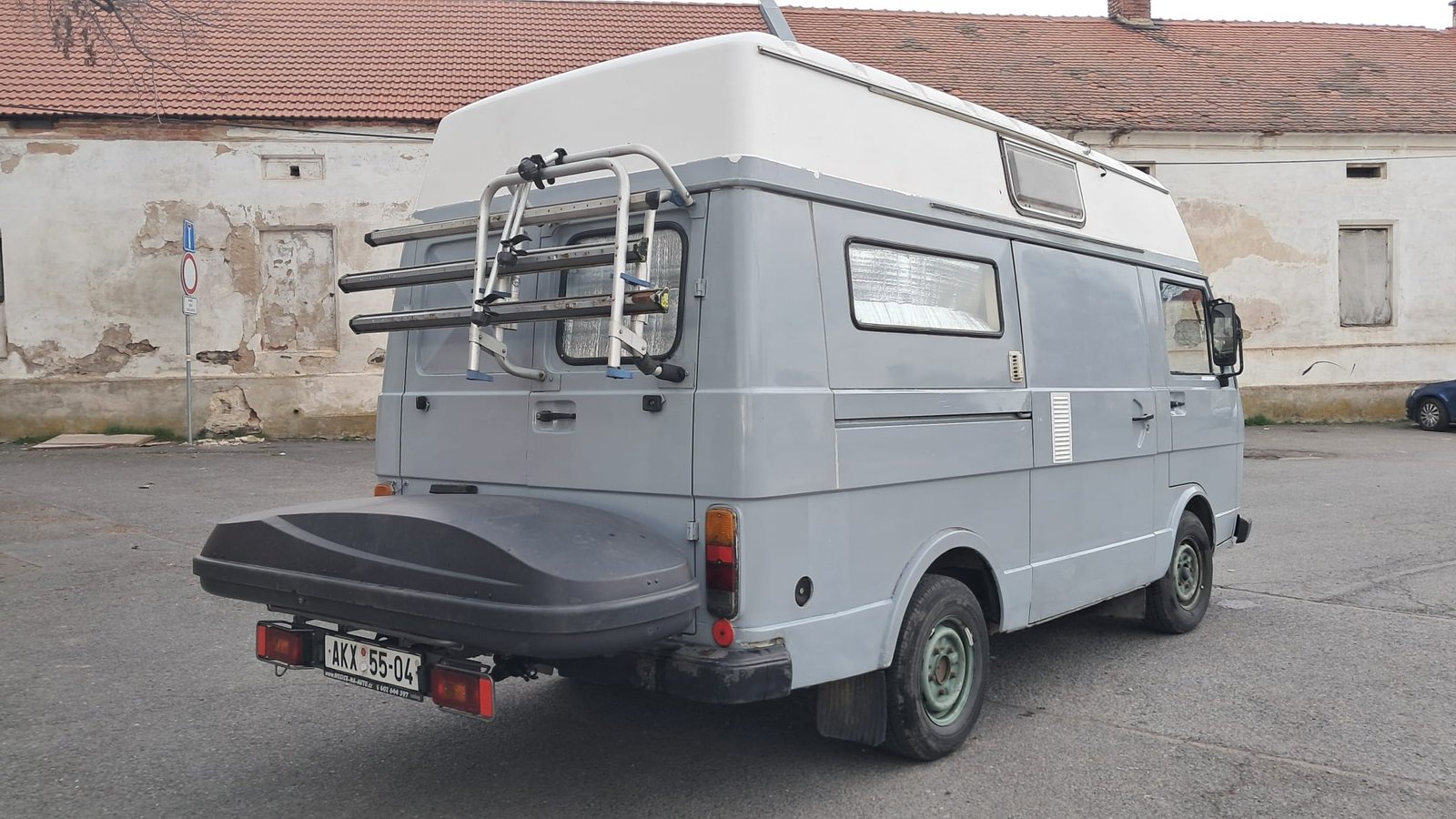 Obytné auto se střešními okny, šedé barvy, parkované na dvoře. Bez viditelné značky a modelu.