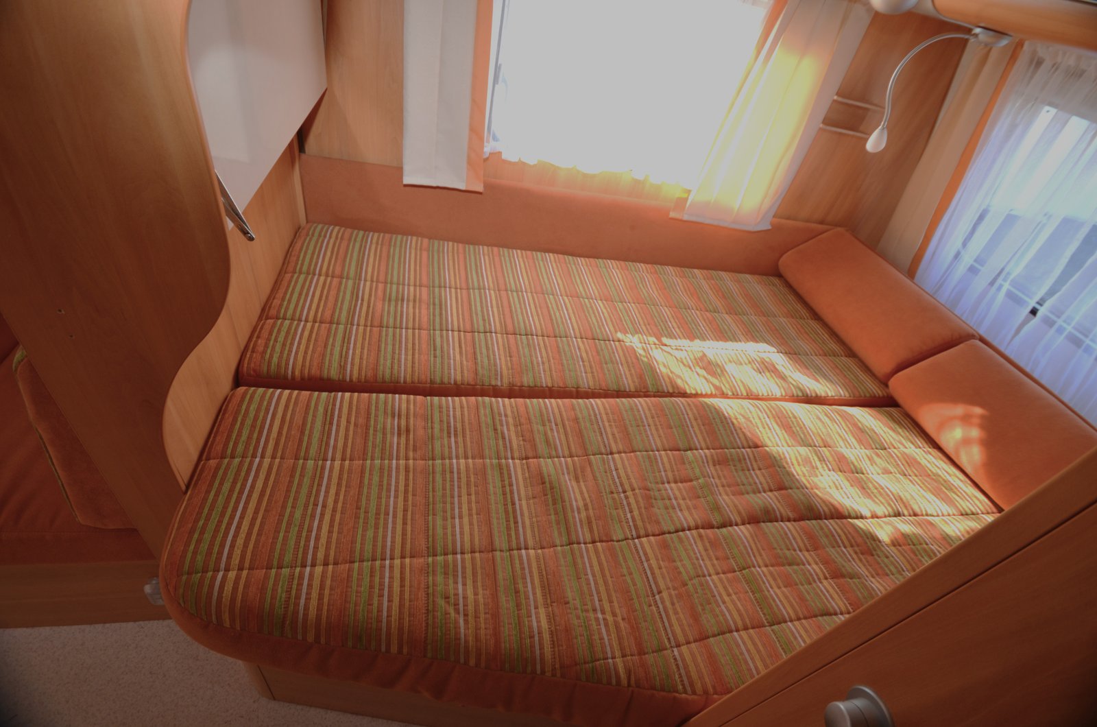 Interiér karavanu s pohodlnou postelí a příjemnými barvami pro relaxaci a odpočinek.