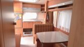 Interiér karavanu s příjemným sezením a kuchyní, ideální pro pohodové cestování a kempování.