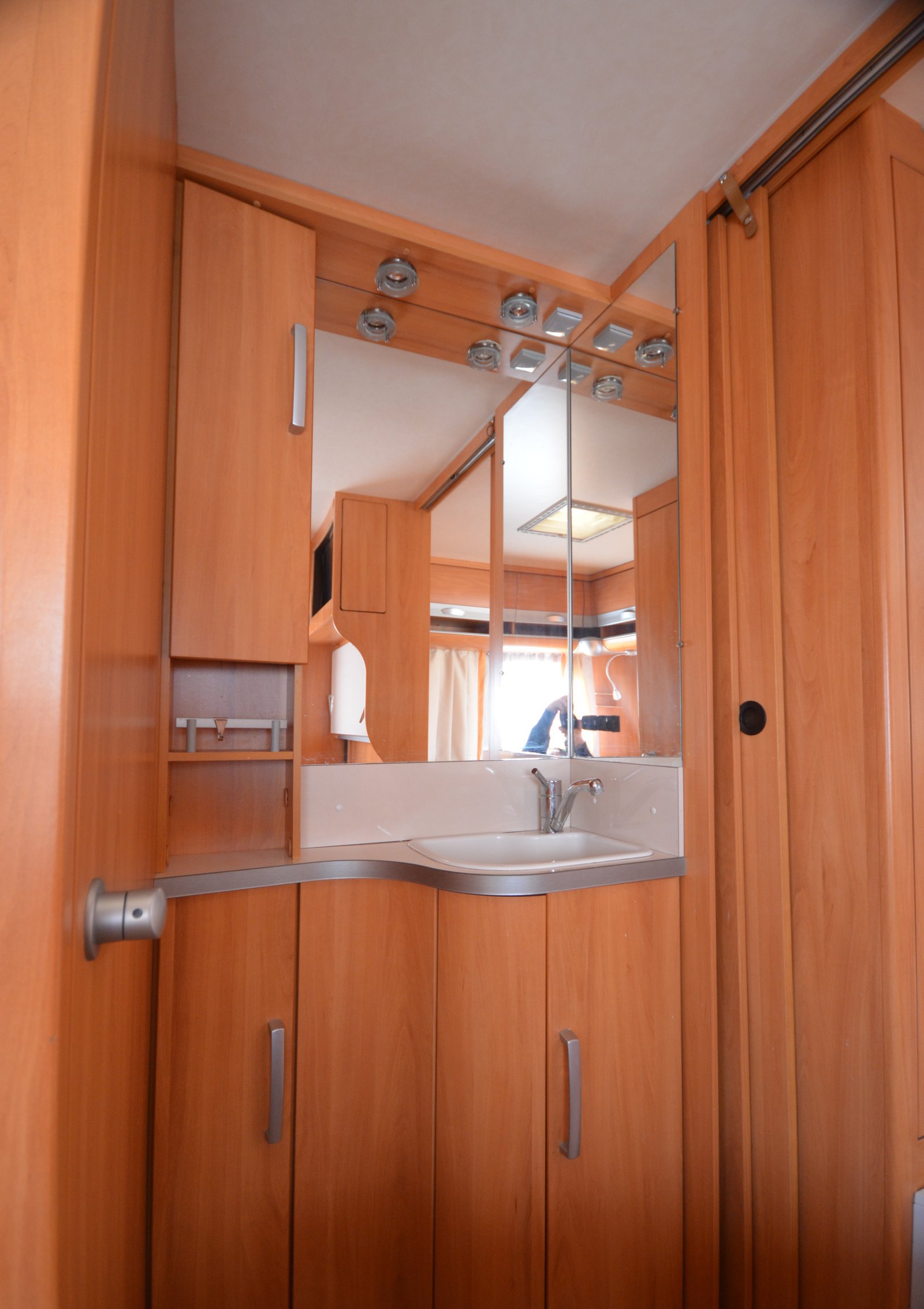 Obrázek interiéru obytného vozu s dřevěným nábytkem a umyvadlem. Ideální pro pohodlné cestování.