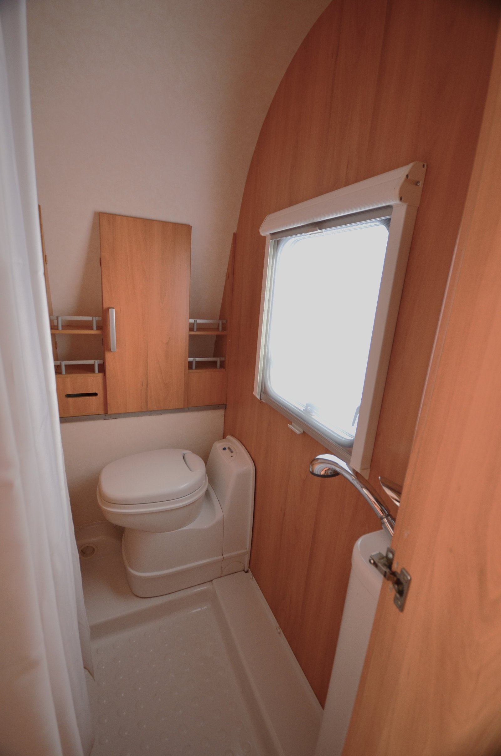 Obrázek interiéru karavanu s koupelnou, skřínkami a sprchou. Prostorný a praktický design pro pohodlné cestování.