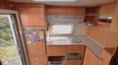 Kuchyňka v karavanu s dřezem, lednicí a úložnými prostory. Příjemné dřevěné detaily pro pohodlné vaření na cestách.