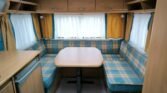 Interiér karavanu s obývacím prostorem, modro-žluté koberce a stůl pro příjemné posezení. Ideální pro dovolenou.