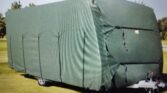 Karavan pokrytý zelenou plachtou, neznámá značka a model. Ideální ochrana před povětrnostními vlivy.