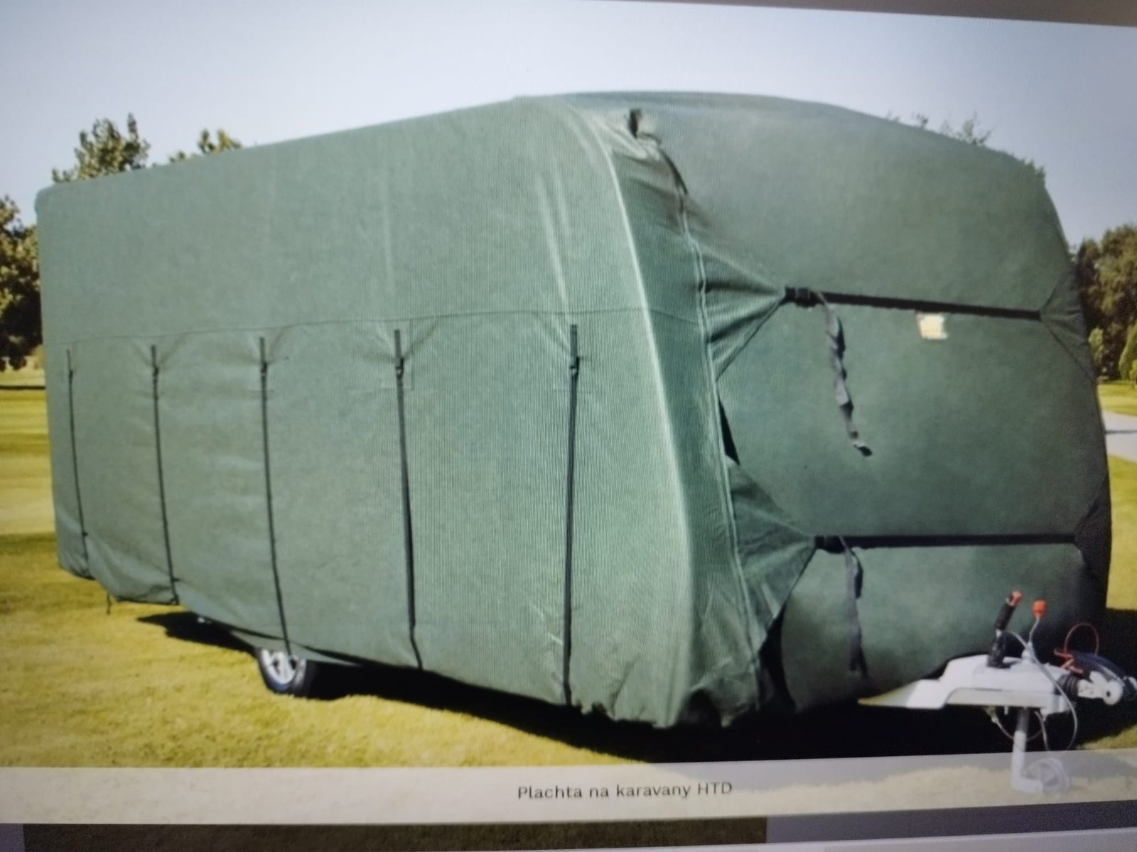 Karavan pokrytý zelenou plachtou, neznámá značka a model. Ideální ochrana před povětrnostními vlivy.